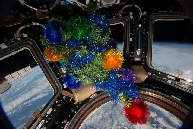Astronauts celebrate Christmas on the International Space Station with colorful decorations inside the Cupola module, which offers breathtaking views of Earth. This image can illustrate festive occasions in space, show space missions, or be used in holiday-themed content related to science and technology.