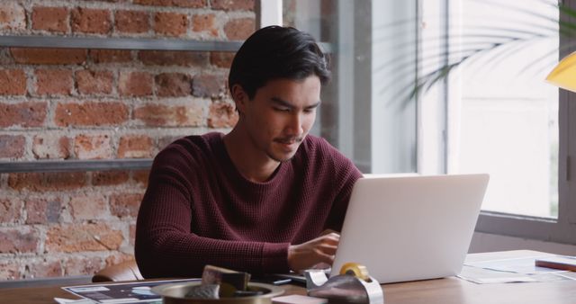 Young Man Working on Laptop in Modern Office with Brick Wall - Download Free Stock Images Pikwizard.com