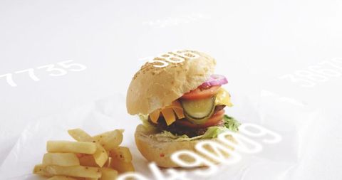 Stacking cheeseburger with pickles and melted cheese, fries on parchment flatlay minimal