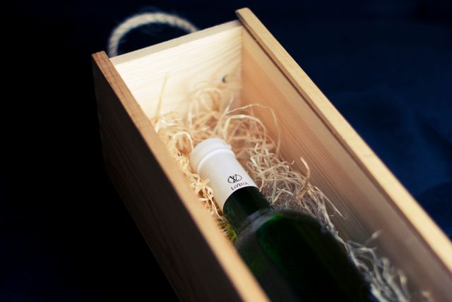 Elegant presentation of a wine bottle in wooden box partially covered by straw bedding. Perfect for use in promotions, e-commerce, wine-related advertisements, luxury gift marketing, or as a product display in catalogs.