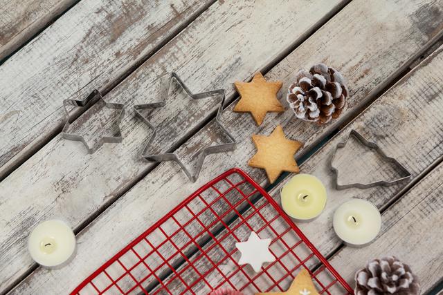 Christmas cookie cutters in star and tree shapes, pine cones, and tealight candles on wooden planks create a cozy and festive atmosphere. Ideal for holiday baking themes, Christmas decorations, and winter-themed projects.