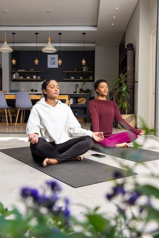 Diverse women meditating at home on sunlit yoga mats for mindfulness and wellness
