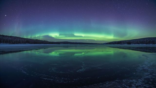 Dancing emerald aurora stretching across frozen lake reflecting starry night sky