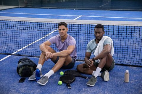 Two athletic men resting on bright blue paddle tennis court with paddles and water bottles