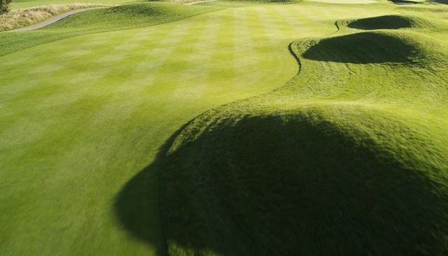 Striped fairway with undulating grassy dunes casting long shadows on bunkers and turf contours