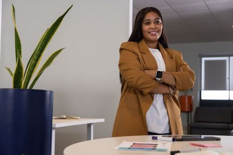 Confident african american businesswoman standing arms crossed at modern office roundtable