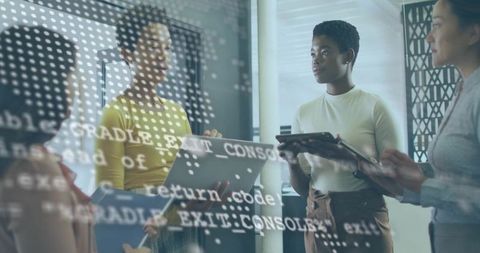 Diverse women reviewing code in modern office with laptops, tablets and code overlay