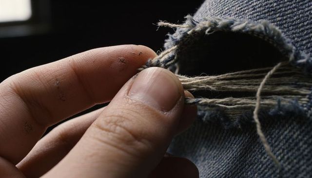 Ink-specked male hand holding frayed denim threads macro close-up of worn jeans