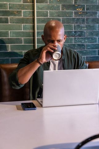 African american man working on laptop while sipping coffee in modern cafe booth