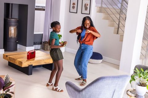African american mother and teenage daughter dancing in modern living room to retro radio