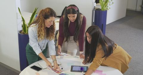 Diverse women collaborating over color swatches and tablet in modern office