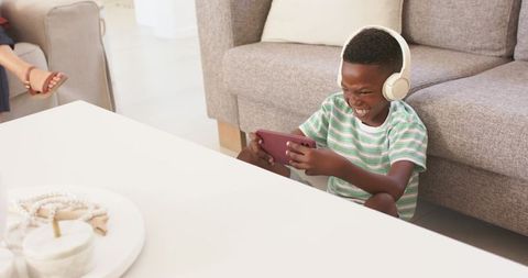 Young boy enjoying mobile gaming with headphones, smiling on living room floor