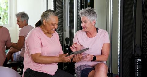 Senior Women Engaging in Fitness Conversation with Tablet in Home Gym