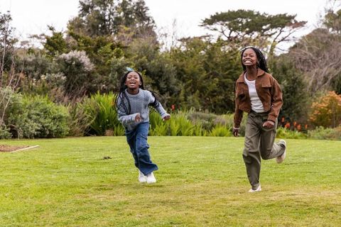 Two african american preteen girls running and laughing across green park lawn during fall