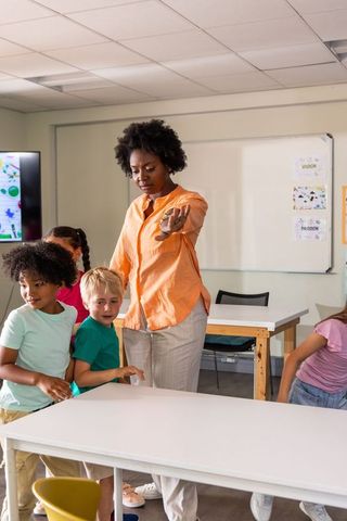 African american teacher pointing and instructing elementary students in modern classroom