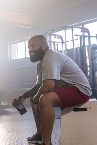 African american athlete resting on plyometric box after workout holding shaker bottle