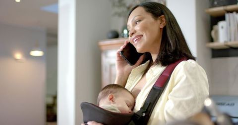 Mother multitasking with baby in carrier at home