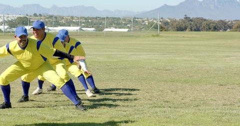 Baseball Team Practicing Fielding Drill in Yellow Uniforms on Grass Field with Mountain Backdrop