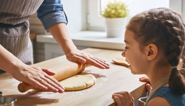 Parent rolling dough while child watches happily during sunny home baking moment