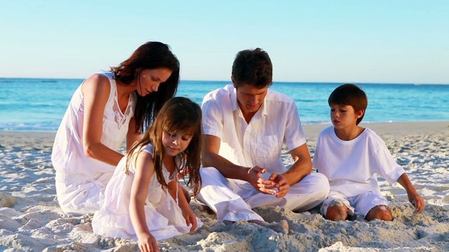 Family enjoying quality time sitting on the sandy beach with ocean background. Perfect for illustrating family vacations, leisure activities, or lifestyle articles focused on family bonding and beach holidays.