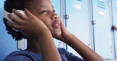 Male student listening to music with headphones in school hallway by lockers