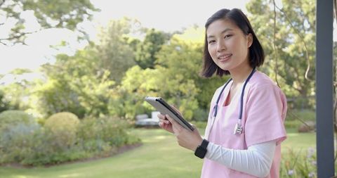 Nurse Standing in Garden with Tablet Providing Home Care Assistance