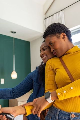 Smiling diverse friends taking cozy mustard-sweater selfie in contemporary home