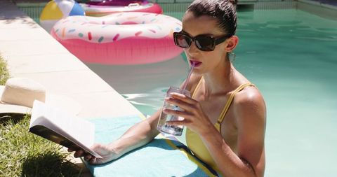 Woman relaxing poolside in summer with treats and book