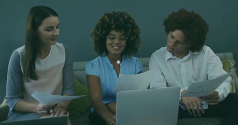 Small team collaborating over laptop and documents on lounge sofa for project planning