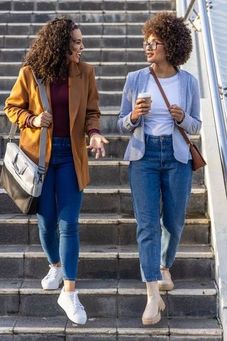 Two african american women walking down urban stairs talking over coffee during commute