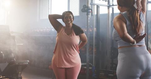 Plus-size black woman and friend stretching and smiling in gym, body positive fitness moment