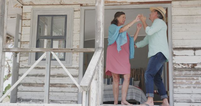 Two senior individuals enjoying a lively dance on the porch of a charming, weathered wooden cabin. Clad in casual attire, they exude joy and companionship. The setting evokes a sense of serene country living and a carefree lifestyle. Ideal for use in advertisements or promotions for retirement planning, lifestyle products, senior activities, or country-themed content.