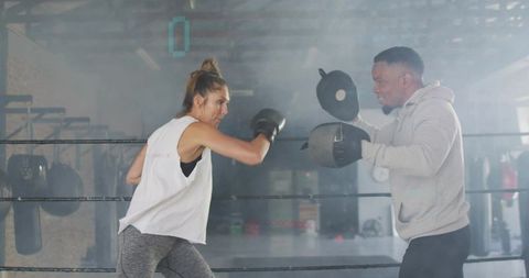 Female boxer landing punch during mitt training with coach in boxing ring