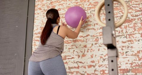 Woman pressing purple medicine ball against brick wall during strength and core workout
