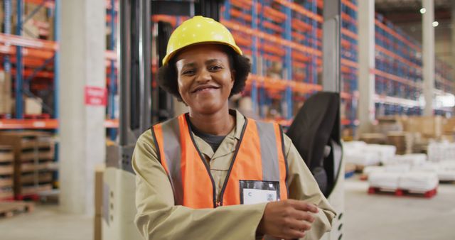 Portrait of african american female worker wearing safety suit and smiling in warehouse. global business, shipping and delivery.