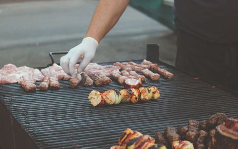 Cook arranging skewers and sausages on large outdoor grill at street barbecue