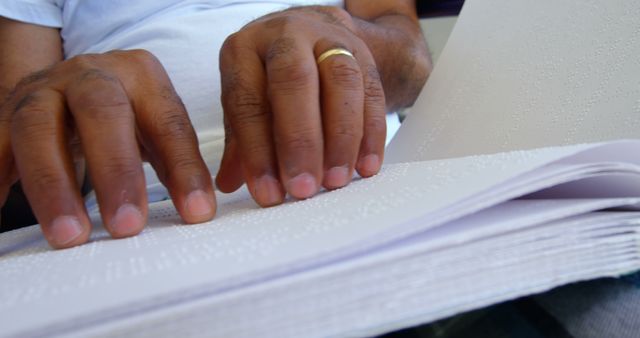 Close-up of blind senior man reading braille book in a comfortable home. He is touching his finger on braille code 4k