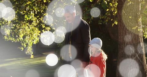 Parent and child walking hand in hand in sunlit park with bokeh lights