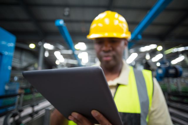This image shows a factory worker using a digital tablet in an industrial environment, illustrating the integration of technology in modern manufacturing. Ideal for use in articles and presentations about industrial automation, digital transformation in manufacturing, and workplace safety.
