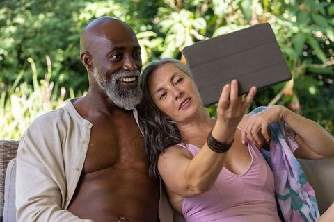 Mature interracial couple enjoying tablet together on garden sofa relaxed outdoor romance