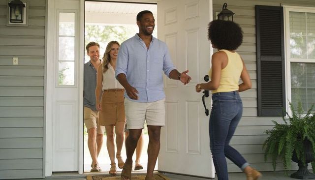 Smiling host greeting friends on sunny front porch during casual summer visit and welcome