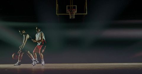 Two basketball players dribbling and defending under dramatic lighting with spotlight