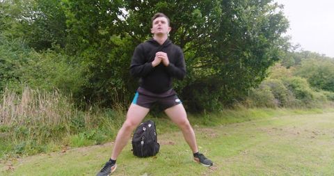 Man exercising outdoors performing squats on grassy path