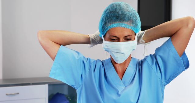 Nurse adjusting her surgical mask in a medical setting. She is preparing for a procedure, focusing on ensuring sanitary conditions. This can be used in health and medical articles, patient care materials, or healthcare industry promotions.