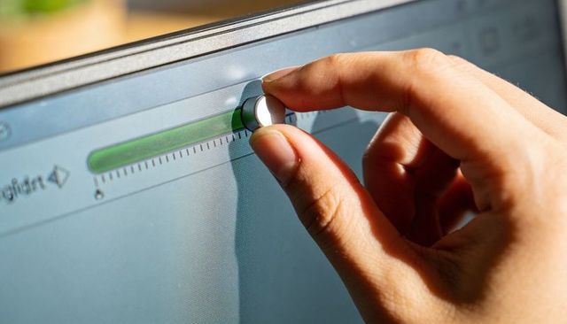 Right hand adjusting magnetic control knob on computer monitor with green progress bar