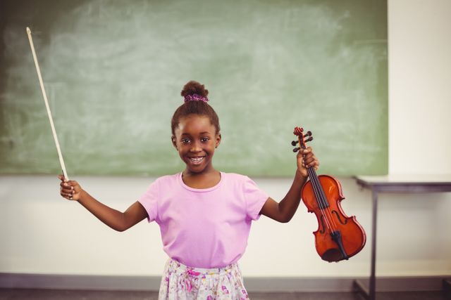 Portrait of smiling schoolgirl holding violin in classroom at school