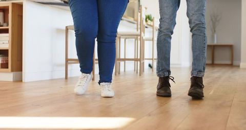 Couple walking on wide-plank hardwood in sunlit open kitchen, casual footwear