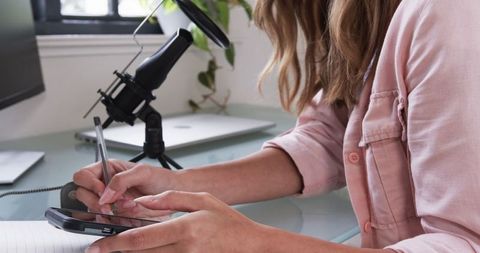 Woman taking notes with smartphone and stylus at modern desk