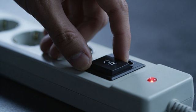 Pressing Off Switch on Power Strip with Glowing Red LED, Hand Turning Off Power