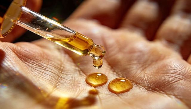Golden facial oil droplets falling from glass dropper onto open palm macro skincare ritual